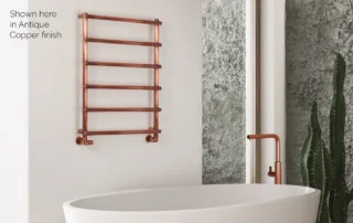 Antique copper wall-mounted towel radiator next to freestanding bath in modern bathroom