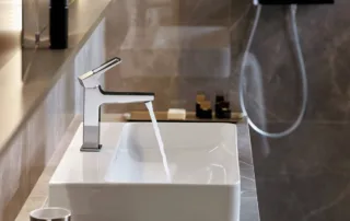 Modern chrome basin mixer tap with loop handle and white countertop basin in hotel-style bathroom
