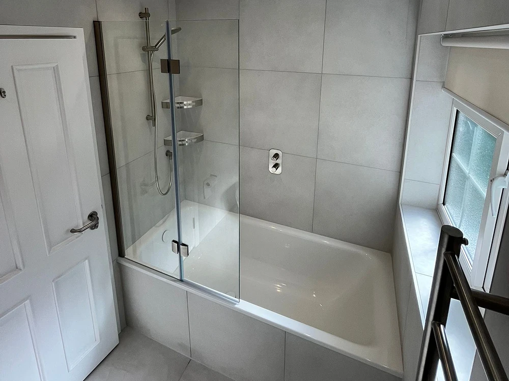 Contemporary bathroom featuring a white bath with overhead shower and glass screen