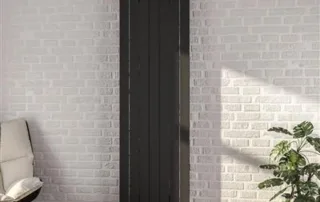 Tall black vertical panel radiator against white brick wall in a contemporary lounge setting