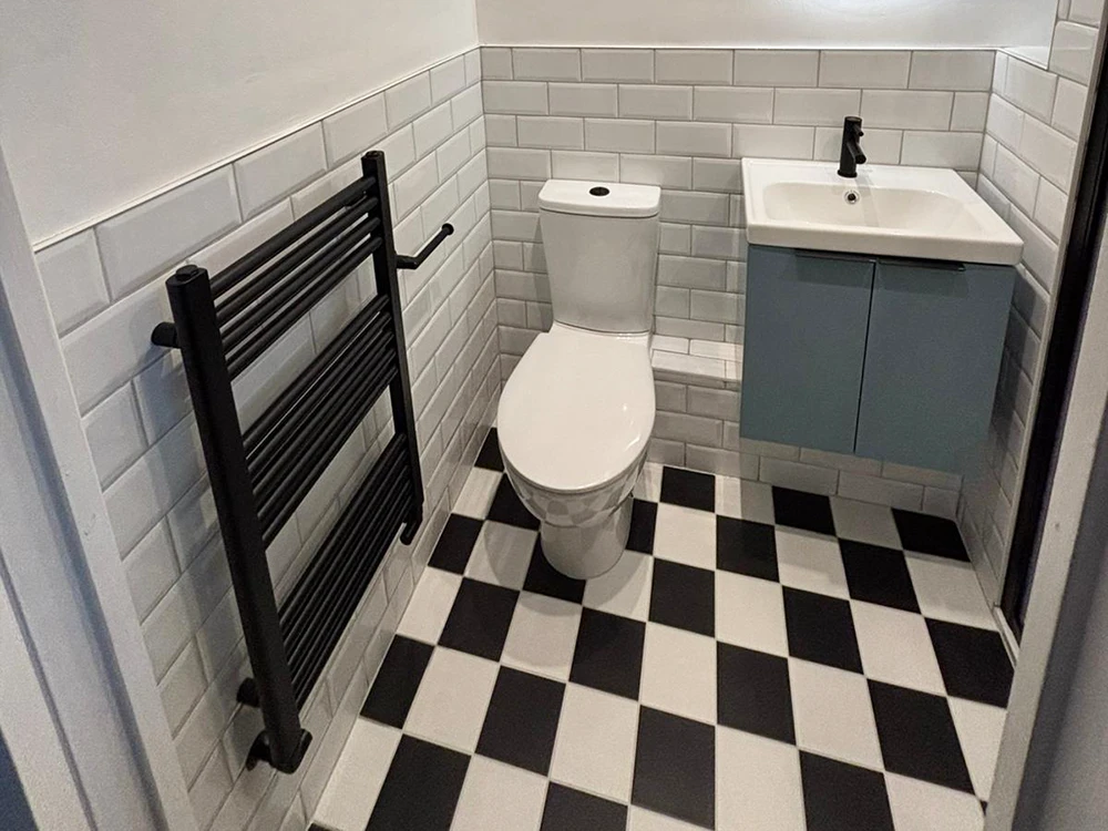 Small bathroom with black towel rail, checkerboard floor tiles, and wall-hung vanity unit