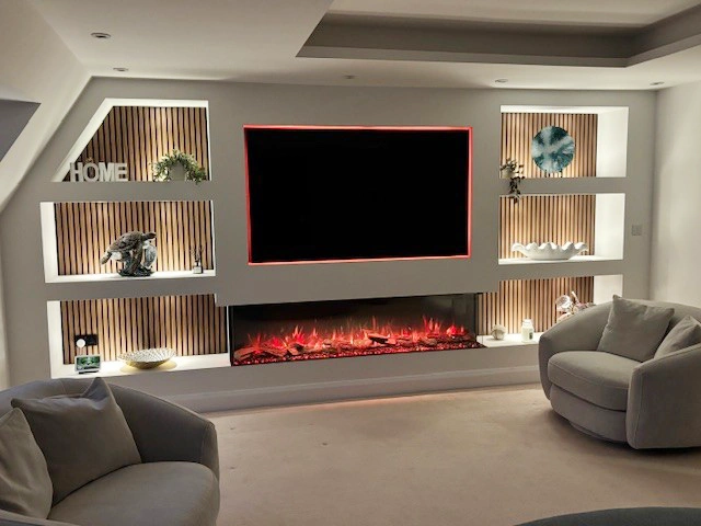 Completed custom media wall with inset electric fire, mounted TV, and illuminated display shelving in a modern living room